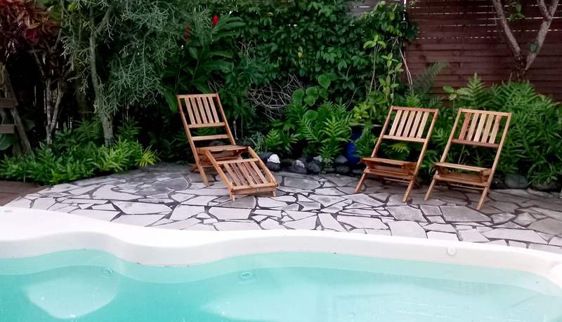 La piscine et ses transats en bois, entourée du jardin tropical