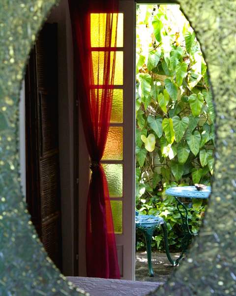 Porte ouvrant sur le jardin, rideau rouge et petite table