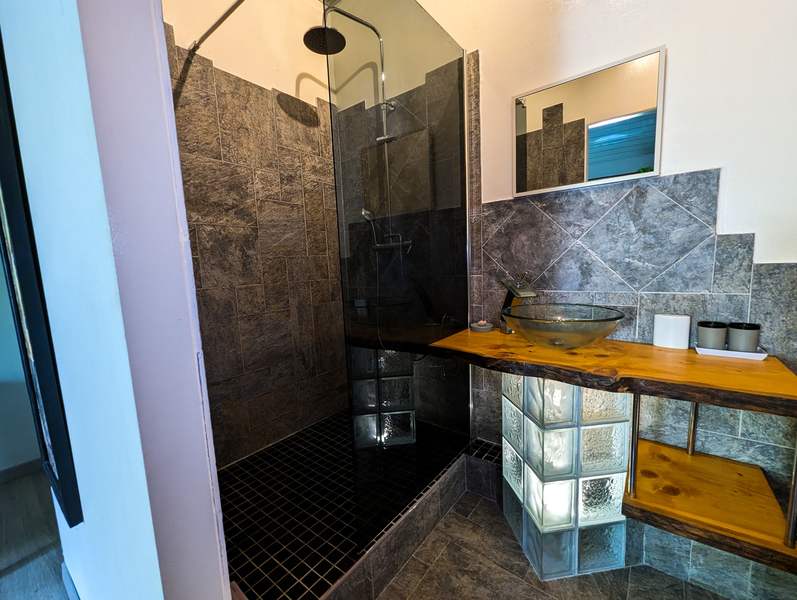 Salle d'eau privative : douche à l'italienne en pierre grise, vasque en verre sur plan en bois massif