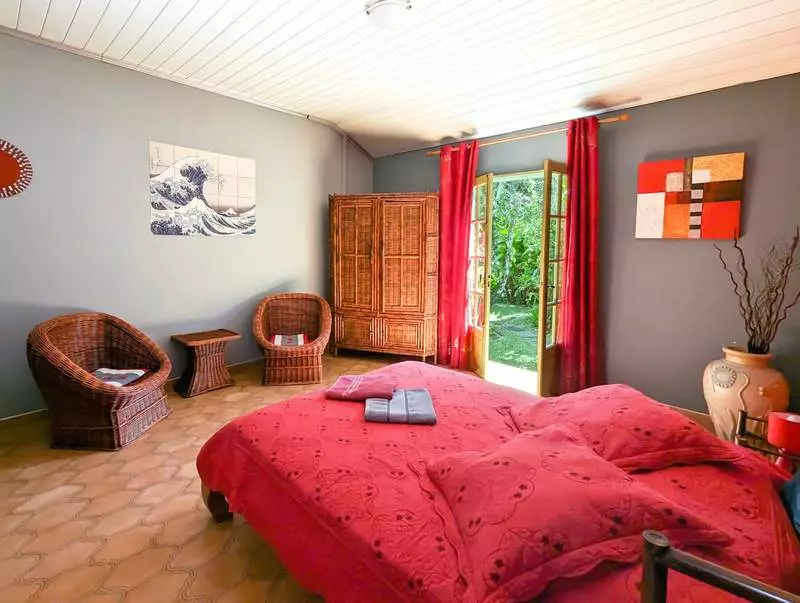 Le lit double aux tons rouges de la chambre Vanille, fenêtre ouverte sur le jardin